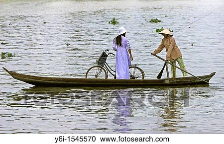 Woman in conical hat paddlling woman in ao dai with bicycle in ferry boat across Mekong Delta river Vietnam View Large Photo Image Stock Image - Woman in conical hat paddlling woman in ao dai with bicycle in ferry boat across Mekong Delta river Vietnam. Fotosearch