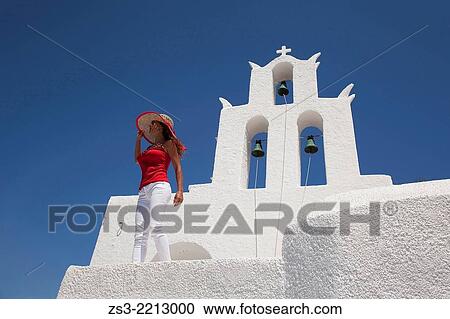 Stock Image - Woman in front of a church bell, Byzantine church of Agia Irini near the Ormos harbour, Ios, Cyclades Islands, Greek Islands, Greece, Europe.. Fotosearch