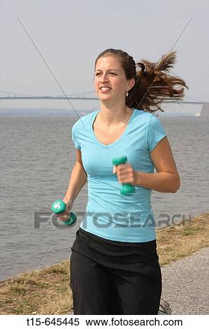 Stock Photography - Woman in her 20's enjoying jogging with weights along a river bank. Fotosearch
