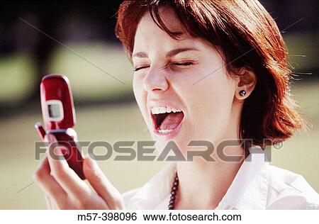Stock Photograph - Woman in her 20s screaming with eyes closed at a flip top mobile phone. Fotosearch