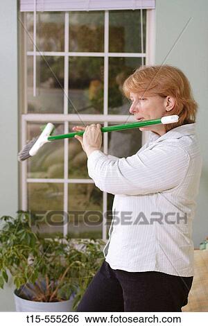 Stock Photograph - Woman in her 40's doing chore and got bored and using the broom as a flute. Fotosearch