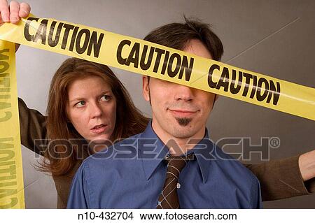 Woman, in her mid-thirties, holding a? CAUTION? sign over the eyes of a man, also in his mid-thirties View Large Photo Image Picture - Woman, in her mid-thirties, holding a? CAUTION? sign over the eyes of a man, also in his mid-thirties. Fotosearch
