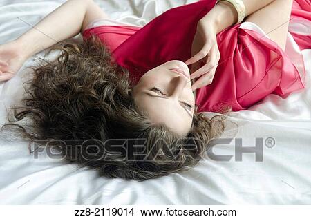 Woman in red dress lying in bed looking away. View Large Photo Image Picture - Woman in red dress lying in bed looking away.. Fotosearch