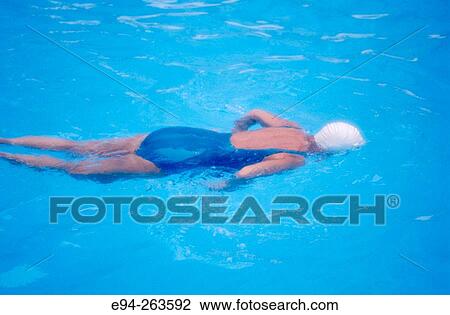 Stock Image - Woman in swimming pool, face down, with white cap & blue suit. Fotosearch