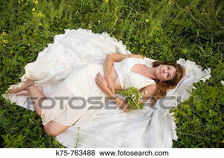 Woman in white dress lying down in a meadow View Large Photo Image Stock Photo - Woman in white dress lying down in a meadow. Fotosearch