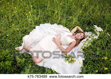 Woman in white dress lying down in meadow with wildflowers View Large Photo Image Stock Photo - Woman in white dress lying down in meadow with wildflowers. Fotosearch