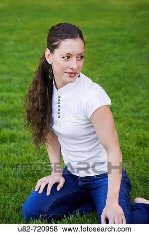 Stock Photo - Woman kneeling on grass lawn in park setting. Fotosearch