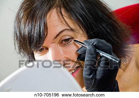 Woman, looking in a hand mirror, applying makeup to her face View Large Photo Image Stock Photograph - Woman, looking in a hand mirror, applying makeup to her face. Fotosearch