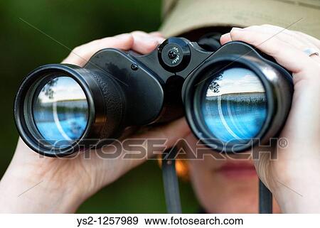 Stock Photo - Woman looking through binoculars with reflection of a lake in the glass. Fotosearch