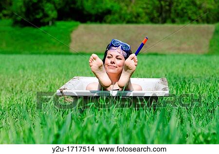 Picture - Woman lying in a bathub on a green field and showing her foot and she have a diving mask. Fotosearch