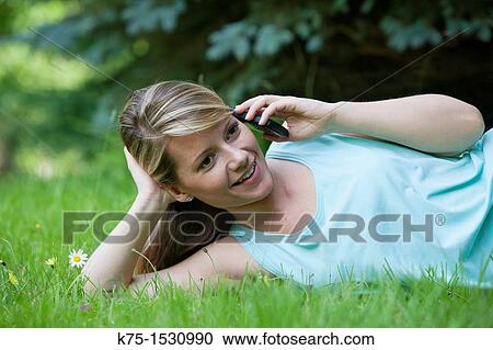 Stock Image - Woman lying on lawn and talking on cell phone. Fotosearch