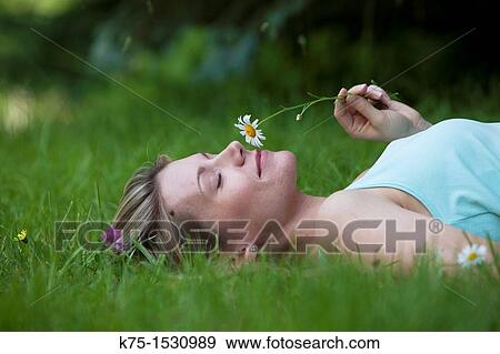 Stock Photo - Woman lying on lawn smelling a daisy. Fotosearch