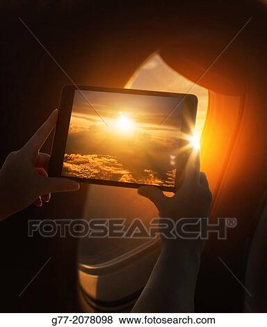 Woman on a plane taking picture of sunset with tablet. View Large Photo Image Stock Photo - Woman on a plane taking picture of sunset with tablet.. Fotosearch
