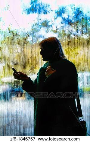 Stock Photo - Woman on cell phone in front of rainy window. Fotosearch