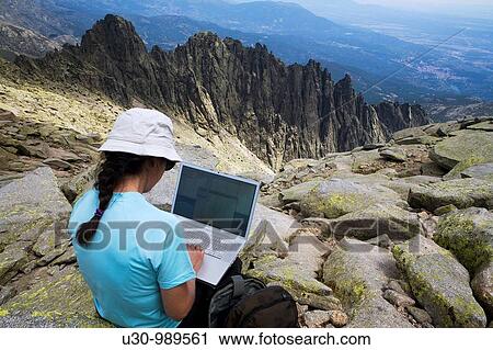 Stock Image - Woman on the summit of La Mira 2 341 m working with a portable computer Mountains of the Sierra de Gredos National Park At the bottom of the image the summits called Galayos Hoyos del Espino? vila Castilla y Le? n Spain. Fotosearch