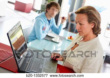 Woman online shopping with laptop computer and son having breakfast in kitchen View Large Photo Image Stock Photo - Woman online shopping with laptop computer and son having breakfast in kitchen. Fotosearch