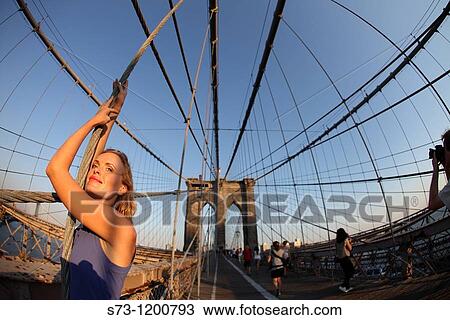 Stock Image - Woman poses at Brooklyn Bridge at sunset, Manhattan, New York, USA. Fotosearch