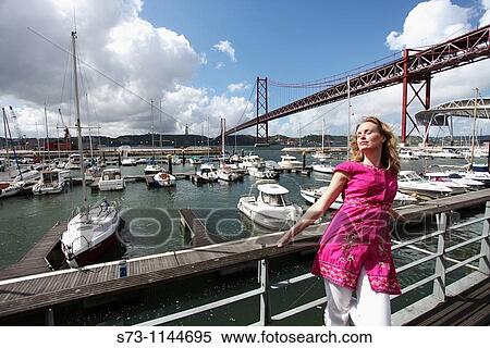 Woman poses with yachts moored at the marina of Doca de Santo Amaro under the Ponte 25 de Abril, Lisbon, Portugal View Large Photo Image Stock Photography - Woman poses with yachts moored at the marina of Doca de Santo Amaro under the Ponte 25 de Abril, Lisbon, Portugal. Fotosearch