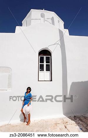 Stock Image - Woman posing in front of a church, Amorgos, Cyclades Islands, Greek Islands, Greece, Europe.. Fotosearch