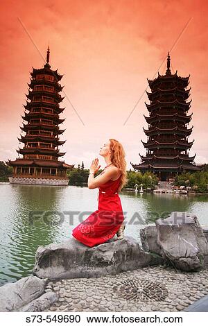 Stock Image - Woman praying next to the twin pagodas of Riming Shuang Ta. Guilin. China.. Fotosearch