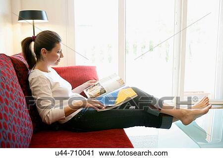 Stock Image - Woman reading a book relaxed on the sofa. Fotosearch