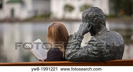 Stock Image - Woman reading next to statue of an Icelandic poet, Tomas Gudmundsson, Reykjavik, Iceland. The city of Reykjavik has been designated as a UNESCO city of literature.. Fotosearch
