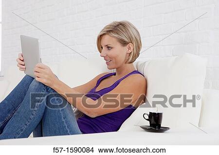 Woman relaxing on her sofa with her tablet computer View Large Photo Image Picture - Woman relaxing on her sofa with her tablet computer. Fotosearch