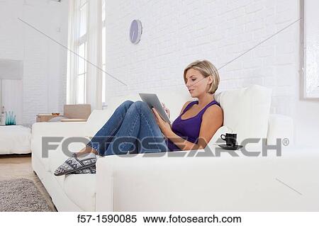 Woman relaxing on her sofa with her tablet computer View Large Photo Image Stock Photography - Woman relaxing on her sofa with her tablet computer. Fotosearch