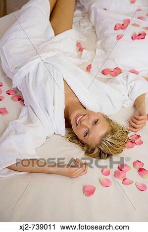 Stock Image - Woman relaxing on the bed with petals. Fotosearch
