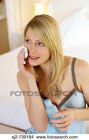 Picture - Woman removing make up with cotton pad and facial lotion. Fotosearch