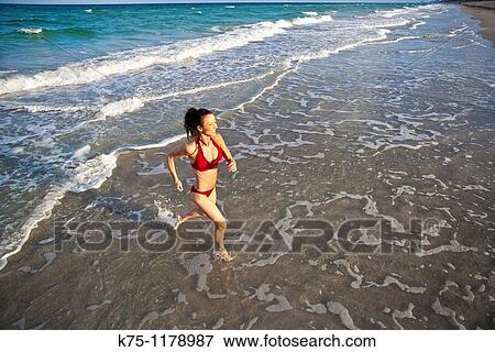 Stock Photo - woman running in shallow water at beach. Fotosearch