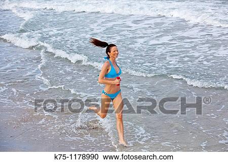 Stock Image - woman running through water at beach. Fotosearch