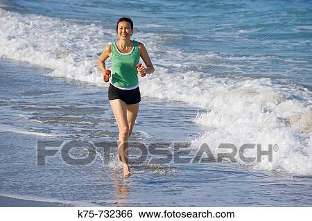 Stock Photograph - woman running with weights at beach. Fotosearch