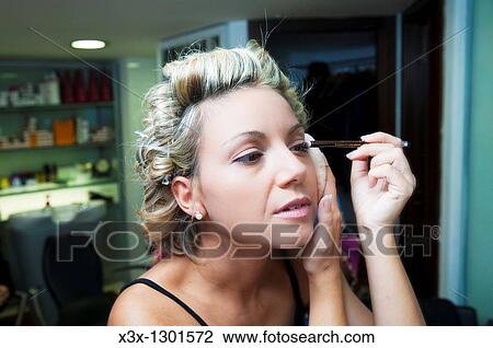 Woman self applying make up in the mirror View Large Photo Image Stock Image - Woman self applying make up in the mirror. Fotosearch