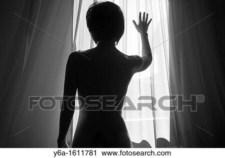 Stock Image - Woman silhouetted against window light placing hand on window. Fotosearch
