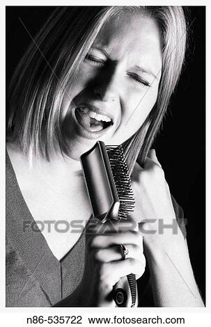 Stock Image - Woman singing into hair brush. Fotosearch