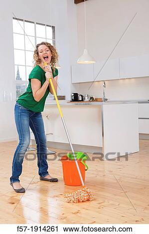 Stock Image - Woman singing while mopping her kitchen floor. Fotosearch