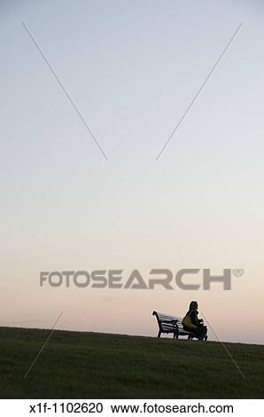 Woman sitting alone by herself on a park bench at twilight, Aberystwyth Wales UK View Large Photo Image Stock Image - Woman sitting alone by herself on a park bench at twilight, Aberystwyth Wales UK. Fotosearch
