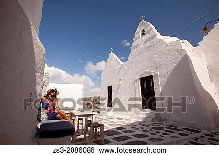 Stock Photograph - Woman sitting at a open-air cafe near Paraportiani Church, Mykonos, Cyclades Islands, Greek Islands, Greece, Europe.. Fotosearch