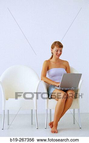 Woman sitting down in a chair working with a portable computer View Large Photo Image Stock Photograph - Woman sitting down in a chair working with a portable computer. Fotosearch