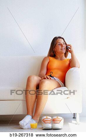 Woman sitting down in a sofa and orange juice and sports shoes on the floor View Large Photo Image Stock Photo - Woman sitting down in a sofa and orange juice and sports shoes on the floor. Fotosearch