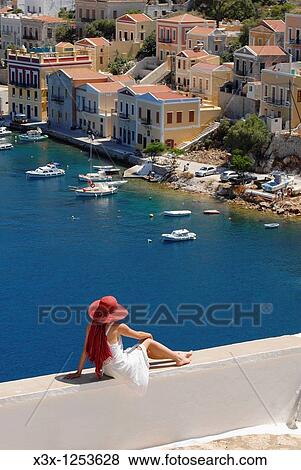 Woman sitting in front of the sweeping view of the island town of Symi Greece View Large Photo Image Stock Photo - Woman sitting in front of the sweeping view of the island town of Symi Greece. Fotosearch