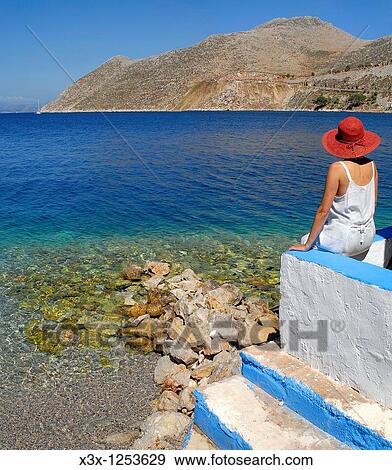 Woman sitting in front of the sweeping view of the waterfront of the island town of Symi Greece View Large Photo Image Stock Photo - Woman sitting in front of the sweeping view of the waterfront of the island town of Symi Greece. Fotosearch