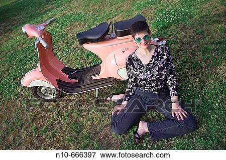 Stock Photo - Woman sitting next to a motor scooter.. Fotosearch