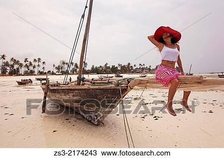 Stock Image - Woman sitting on a dhow at Nungwi beach, Nungwi, Zanzibar Island, Tanzania, Indian Ocean, East Africa.. Fotosearch