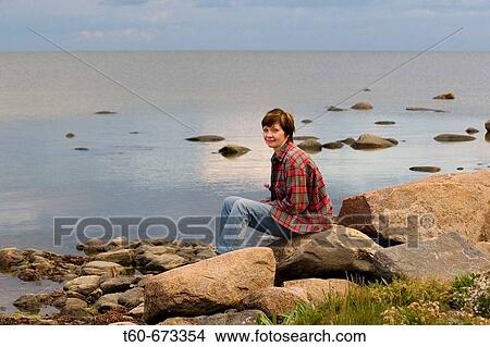 Woman sitting on a rock by the sea View Large Photo Image Picture - Woman sitting on a rock by the sea. Fotosearch