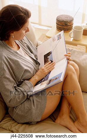 Woman sitting on a sofa reading a book View Large Photo Image Stock Photo - Woman sitting on a sofa reading a book. Fotosearch