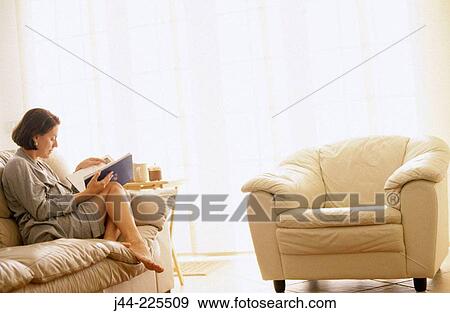 Woman sitting on a sofa reading a book View Large Photo Image Stock Photo - Woman sitting on a sofa reading a book. Fotosearch