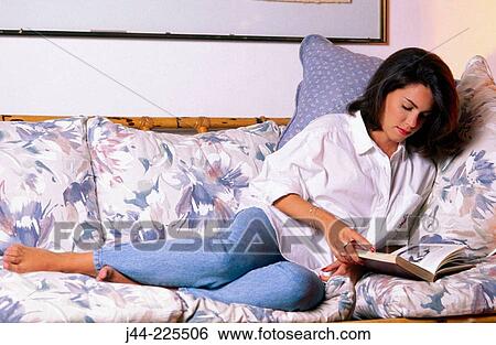 Woman sitting on a sofa reading a book View Large Photo Image Stock Photograph - Woman sitting on a sofa reading a book. Fotosearch