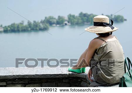 Stock Image - Woman sitting on a wall and watching islands on the water. Fotosearch